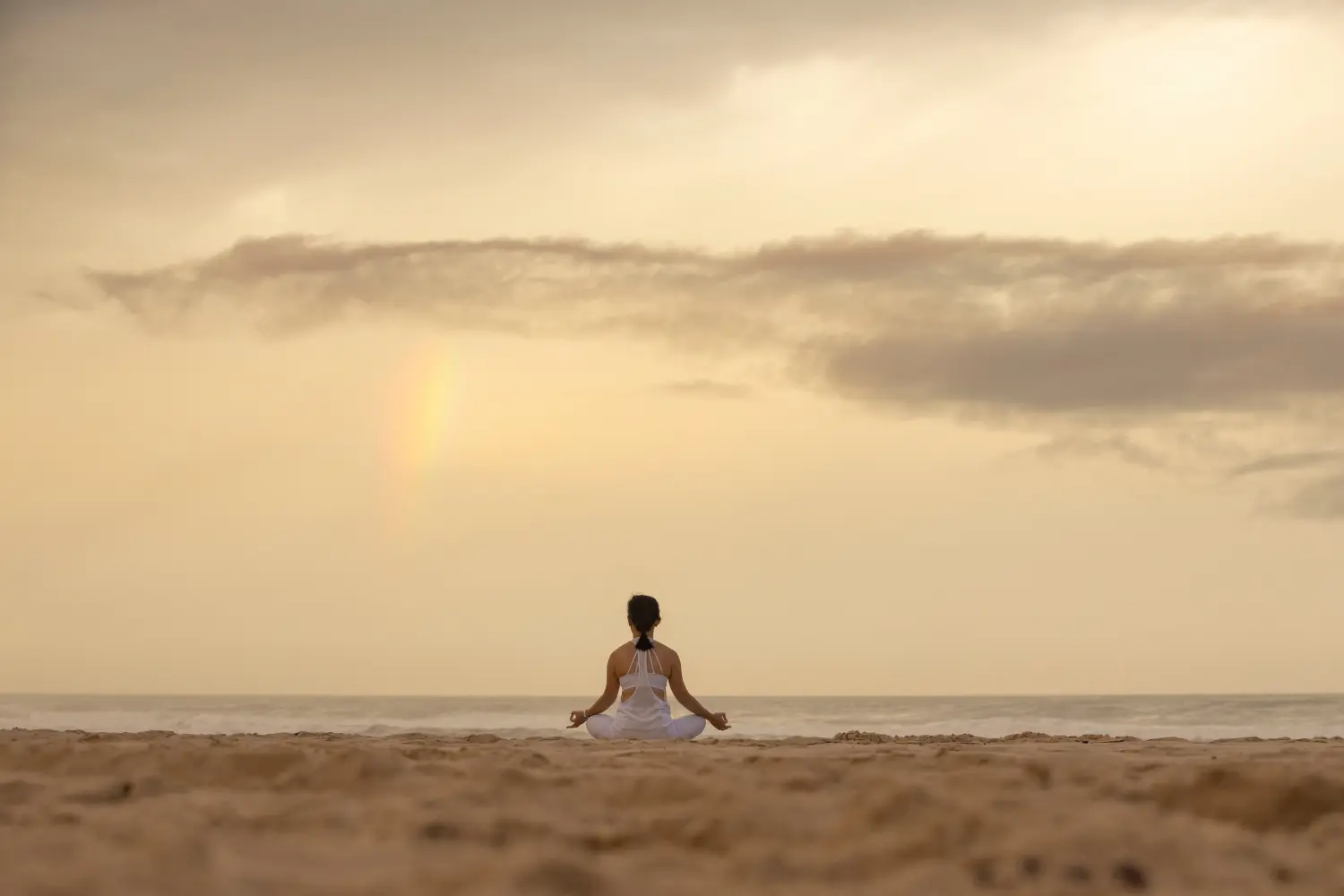Yoga-Lotus-Pose-Meditationspraxis einer jungen asiatischen Frau an einem Strand mit Regenbogenhintergrund.